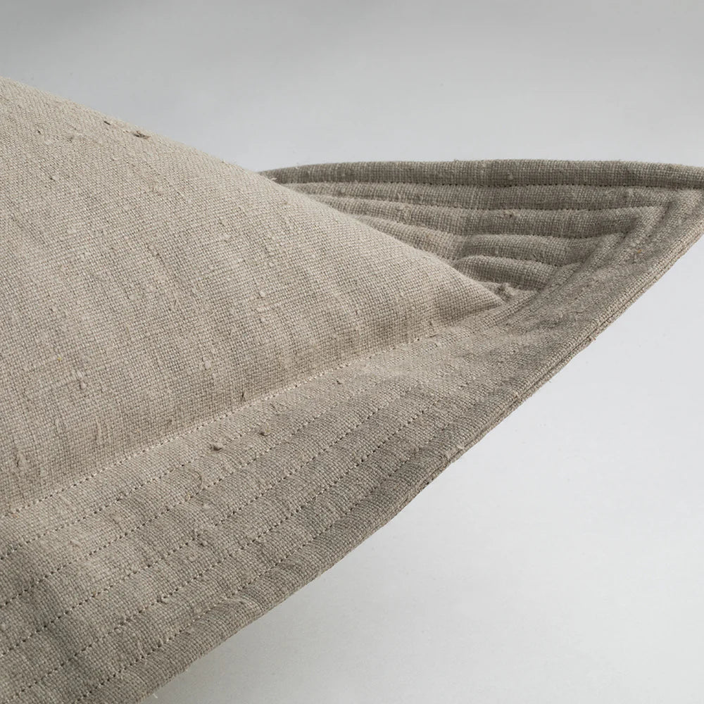 Beige linen quilted edge pillow in cement color with visible stitching and a textured woven surface