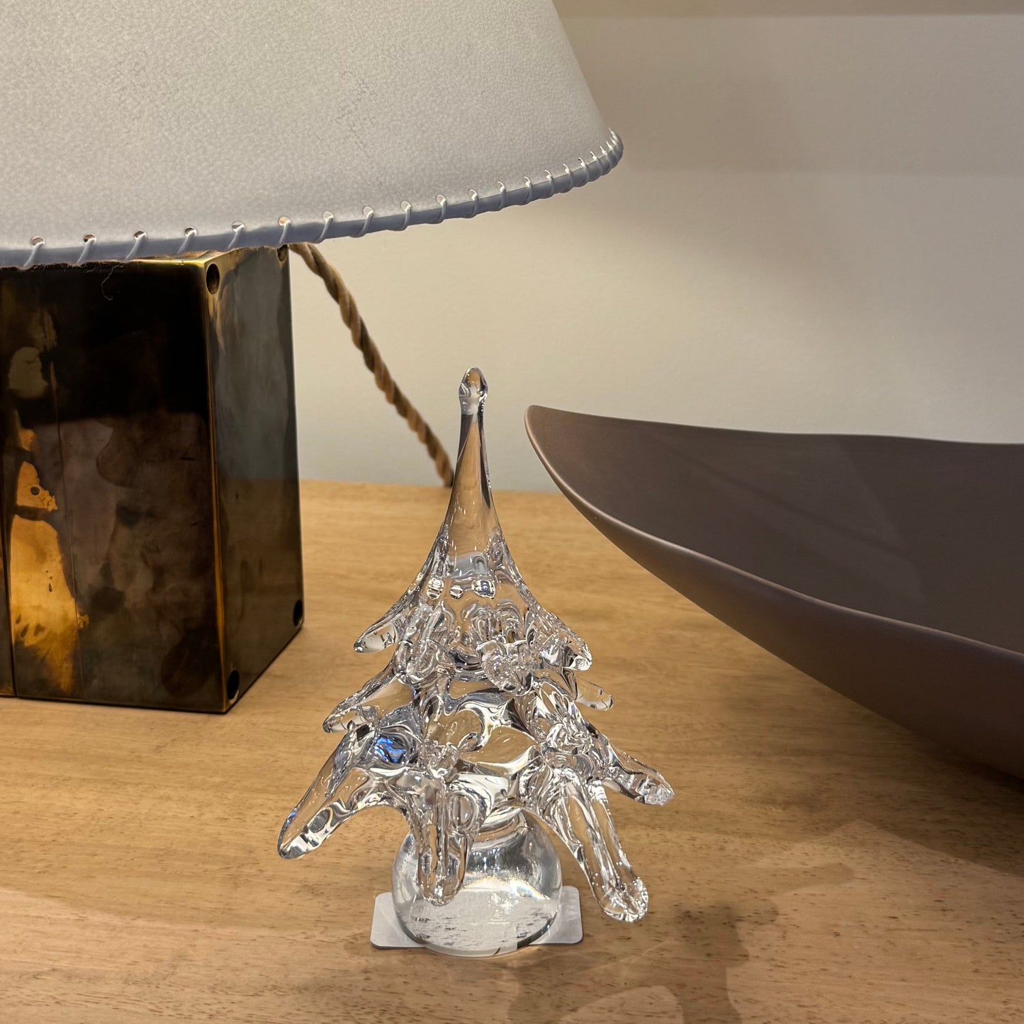 Crystal Christmas tree ornament on a wooden surface with a lamp and decorative bowl in the background.