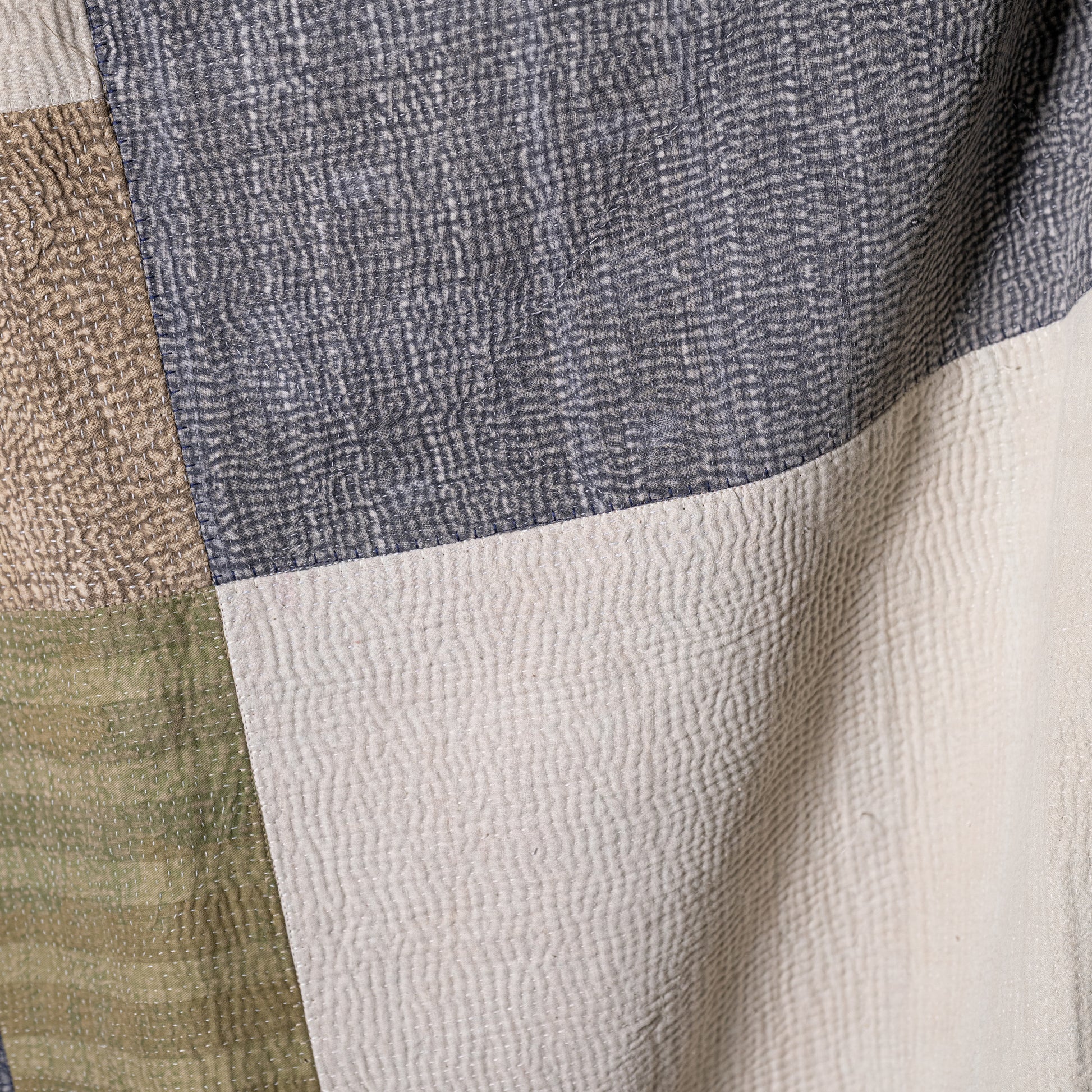 Mosaic quilt featuring textured hand-quilted patchwork panels in muted gray beige and olive green tones