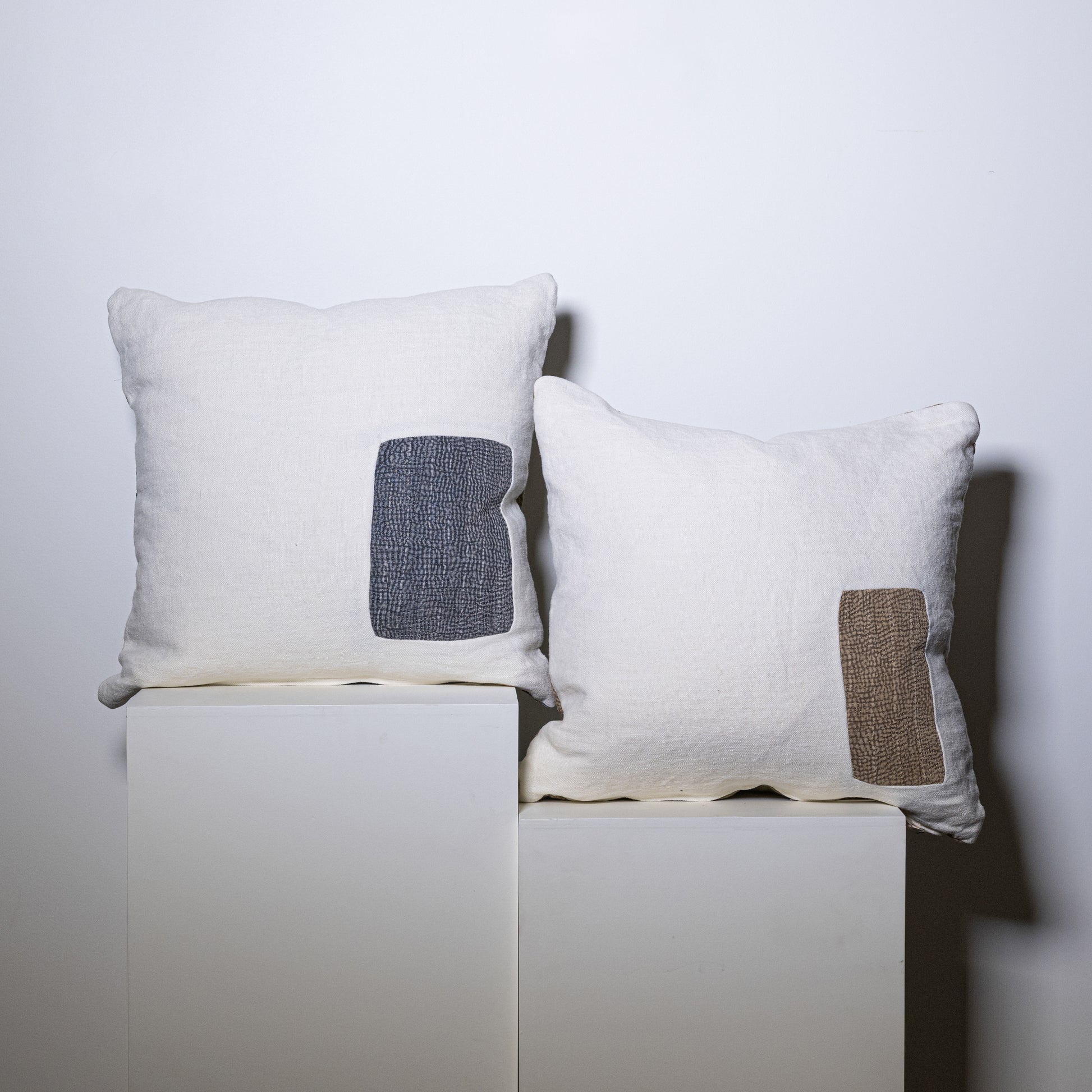 Two off-white linen mosaic pillows with rectangular textured patches in dark gray and beige on the front sides