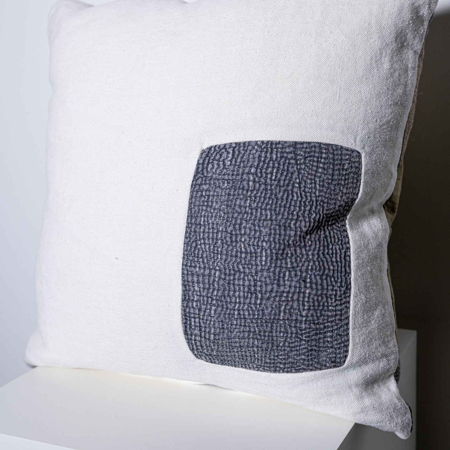 White linen mosaic pillow with a textured gray patch on one side for decorative use