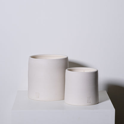 Two minimalist off-white ceramic candle holders with subtle embossed logo base from candle trapper collection