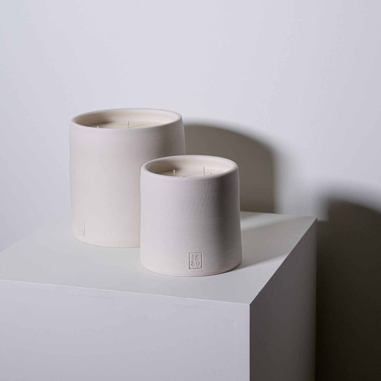 Two minimalist white ceramic candle holders with three-wick matte finish candles and subtle embossed preacher branding