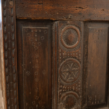 Dark brown wooden panel with intricate carved circular and geometric patterns on 19th century french mountain chest