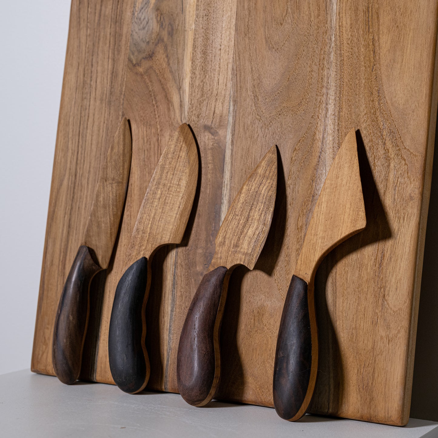 Set of four teak and sono wooden kitchen knives with dark ergonomic handles and natural wood blades on wooden board